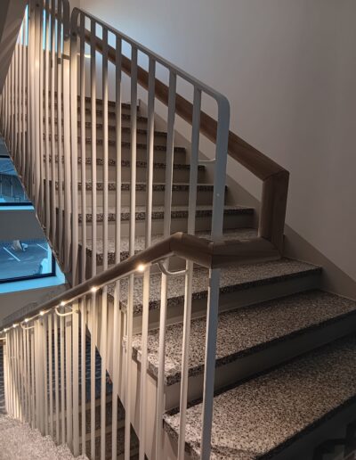 Metallkonstruktsiooniga trepp terrazzo astmete ja puidust käsipuuga.